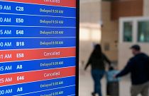 Travellers walk as a video board shows flight delays and cancellations at Ronald Reagan Washington National Airport. 
