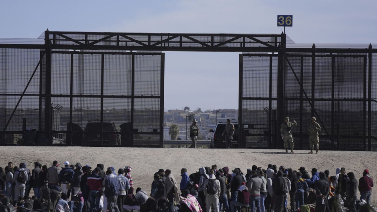 Migrants who crossed the border from Mexico into the U.S. wait next to the U.S. border wall. Seen from Ciudad Juarez, Mexico, March 30, 2023