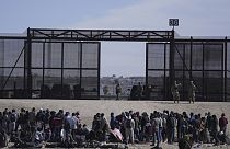 Migrants who crossed the border from Mexico into the U.S. wait next to the U.S. border wall. Seen from Ciudad Juarez, Mexico, March 30, 2023
