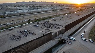 As the sun sets, migrants wait outside a gate in the border fence to enter into El Paso, Texas, to be processed by the Border Patrol, Thursday, May 11, 2023