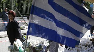 People holding shopping bags full of fruits and vegetables pass a Greek flag during a protest by farmers' market vendors in the northern Athens' suburb of Gerakas.