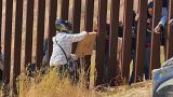 Un repartidor entregando una pìzza desde México a través de los barrotes de la valla fronteriza con EEUU