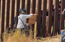 Un repartidor entregando una pìzza desde México a través de los barrotes de la valla fronteriza con EEUU