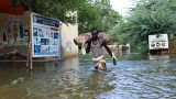 رجل يحمل كيسًا على كتفه وهو يمشي في مياه الفيضانات في بلدوين - الصومال. 2023/05/12