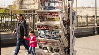 Un grupo de personas pasa junto a un estante con periódicos turcos un día después de las elecciones presidenciales, en Estambul, Turquía, el lunes 15 de mayo de 2023