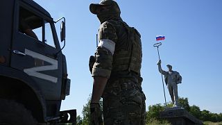 Orosz katona egy orosz katonai teherautó mellett az ukránoktól elfoglalt Mariupolban 2022 júniusában