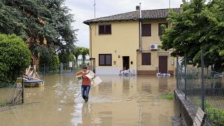 A woman carries her belongings in a flooded area near Bologna, Italy, Thursday, May 18, 2023. 