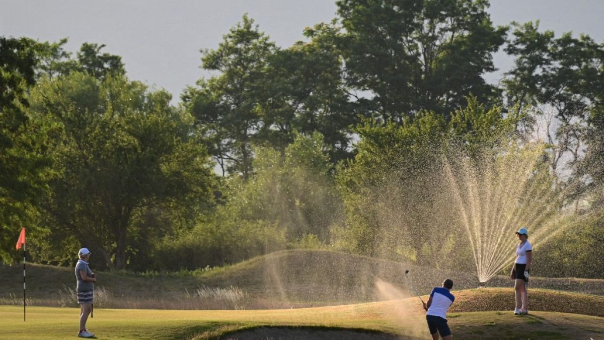 French golfers play in front of active water sprinklers in Rouffach, eastern France, on June 15, 2022.