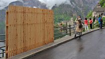 A provisional wooden fence partially blocks the beautiful view, as visitors take selfies with the landscape in the tourist community of Hallstatt. 