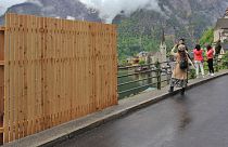A provisional wooden fence partially blocks the beautiful view, as visitors take selfies with the landscape in the tourist community of Hallstatt. 