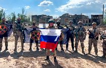 فرمانده گروه واگنر با پرچم روسیه در کنار سربازان مزدور با پرچم واگنر به تاریخ بیستم مه ۲۰۲۳ در شهر باهموت