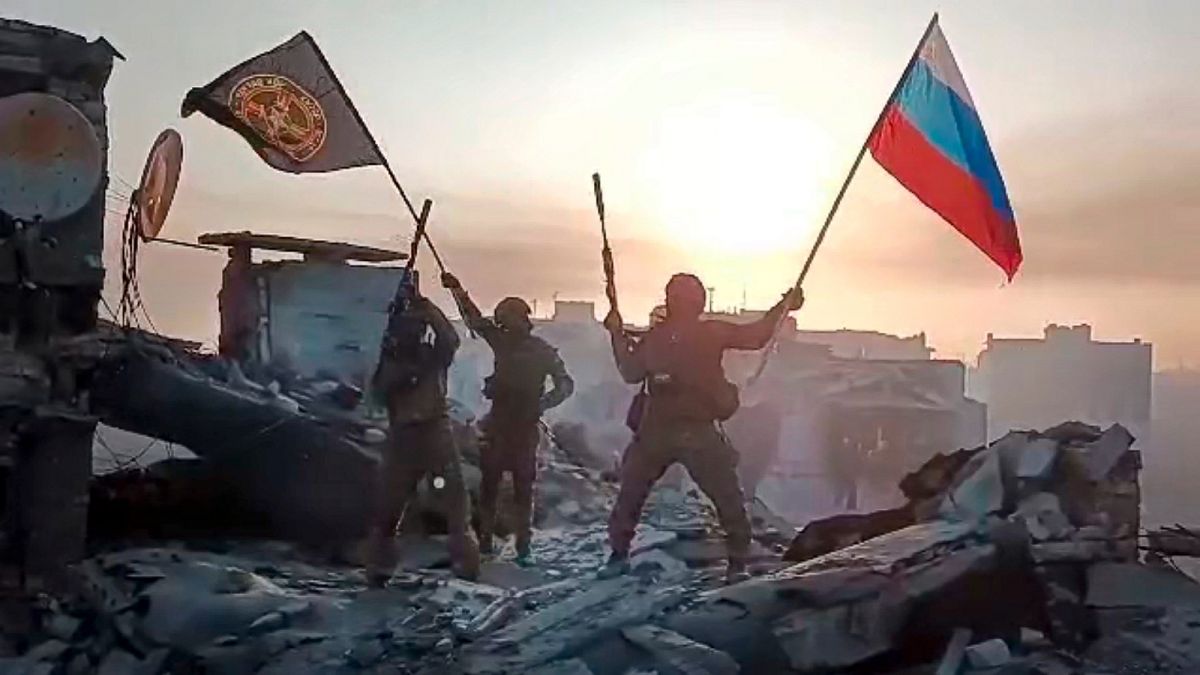 Yevgeny Prigozhin's Wagner Group military company members wave a Russian national and Wagner flag atop a damaged building in Bakhmut, Ukraine.