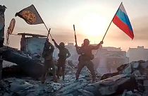 Yevgeny Prigozhin's Wagner Group military company members wave a Russian national and Wagner flag atop a damaged building in Bakhmut, Ukraine.