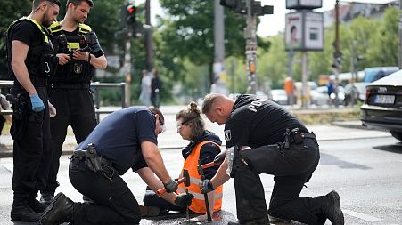 Police officers use hammers and chisels to remove a climate activist who has glued himself to a road during a climate protest in Berlin, Germany, 22 May 2023.