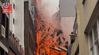 Una pared se derrumba mientras un gran incendio arrasa un edificio de siete plantas.