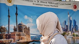 A Turkish woman goes to the polling station as she looks at a banner showing a Turkish mosque and the skyline of Frankfurt, Germany, Wednesday, May 24, 2023.