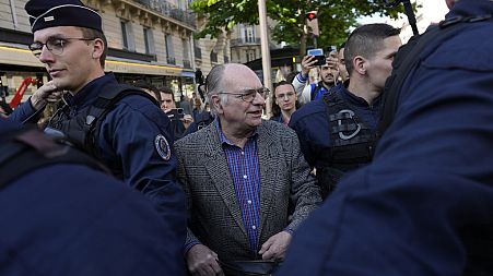 A shareholder is protected by police officers as tries to enter French oil and gas giant TotalEnergies's annual shareholders meeting in Paris.