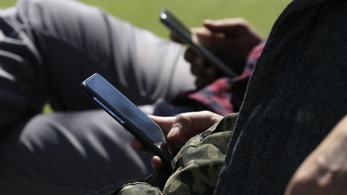 La gente usa sus teléfonos mientras está sentada en un banco del parque en South Park el viernes 13 de abril de 2018, en San Francisco, California