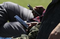La gente usa sus teléfonos mientras está sentada en un banco del parque en South Park el viernes 13 de abril de 2018, en San Francisco, California