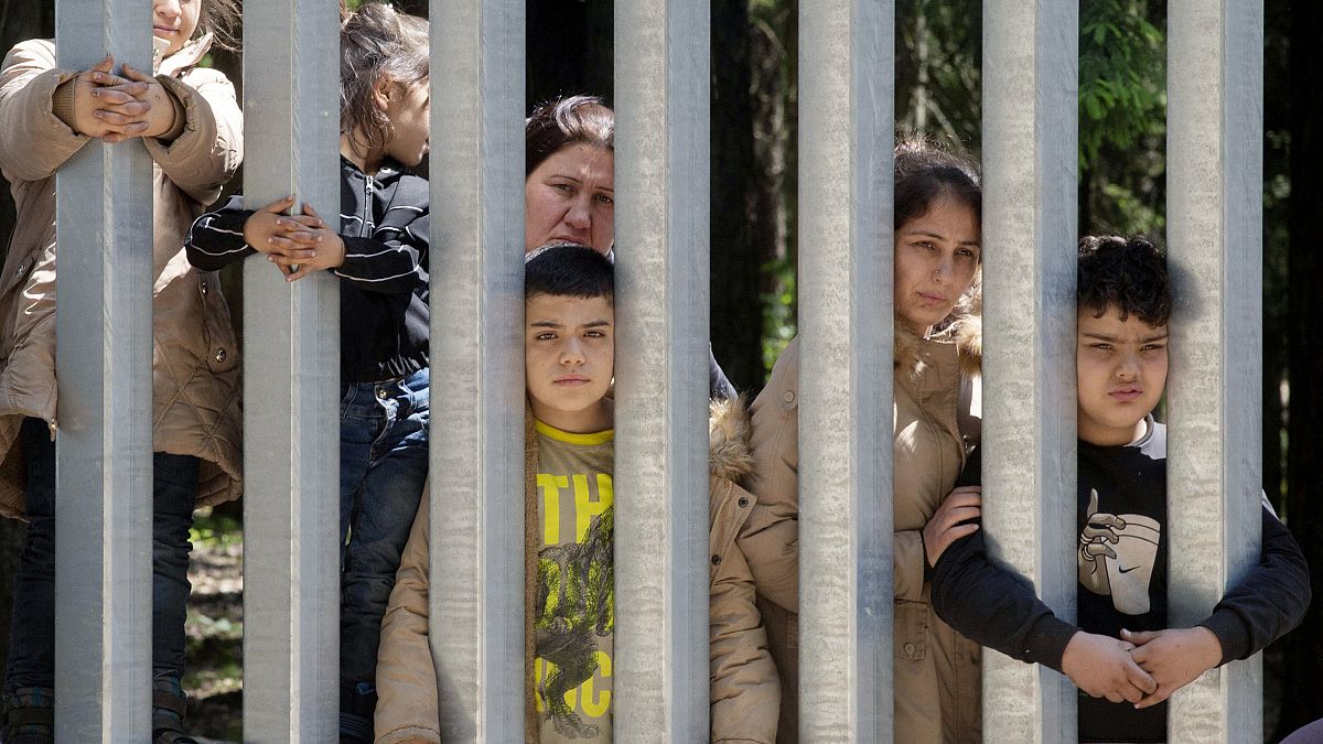 Members of a group of some 30 migrants seeking asylum are seen in Bialowieza, Poland, on 28 May 2023 across a wall that Poland has built on its border with Belarus.