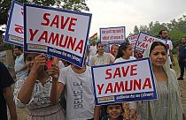 People hold placards as they form a human chain to clean the polluted waters of river Yamuna laden with foam, on the eve of world environment day in New Delhi on June 4, 2023.