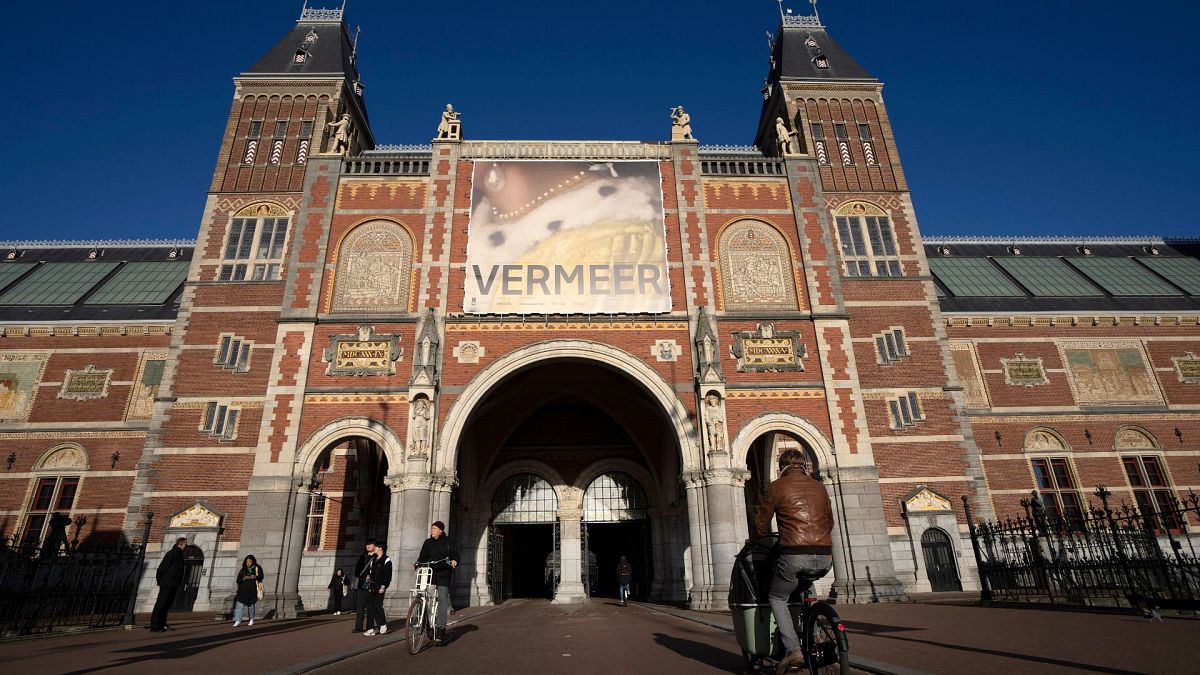 Cyclists pass under the Vermeer exhibit sign at Amsterdam's Rijksmuseum, Monday, Feb. 6, 2023. 