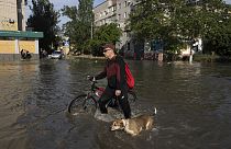 A local resident with a bike and a dog walks along the street past the buildings in Kherson, Ukraine, Tuesday, Jun 6, 202