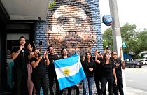 Staff at the Fiorito restaurant hold an Argentinian flag as they pose for a photograph taken by a colleague in front of a mural of Lionel Messi, Wednesday, June 7, 2023, in Mi
