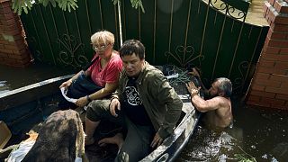 Local residents with their dog are evacuated on a boat from a flooded neighbourhood in Kherson, Ukraine, Thursday, June 8, 2023. 