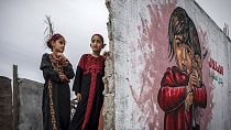 Zwei Mädchen kämmen sich die Haare vor einem Wandbild, die Teil einer Ausstellung im Gazastreifen ist