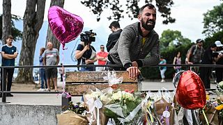 A man reacts in front of flowers and candles for the victims of a stabbing attack that occured the day before in the 'Jardins de l'Europe' parc in Annecy, France.