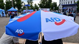 Esta foto tomada el 10 de agosto de 2021 muestra a simpatizantes bajo un paraguas con el logotipo del partido ultraderechista Alternativa Para Alemania.