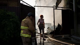 A woman walks out of her burning house as firefighters work to extinguish the fire after a Russian attack in Kherson, Ukraine