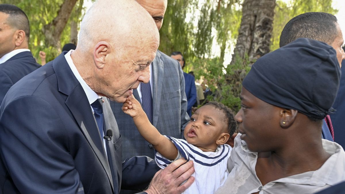 This photo provided by the Tunisian Presidential Palace, shows Tunisian President Kais Saied talking to a migrant and her baby during a surprise visit to a migrant camp.