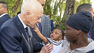 This photo provided by the Tunisian Presidential Palace, shows Tunisian President Kais Saied talking to a migrant and her baby during a surprise visit to a migrant camp.