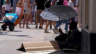 A man sits under an umbrella to shelter himself from the sun while begging for money in the street during hot weather in Madrid, Spain, Saturday, July 16, 2022.