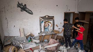 کودکان در خرابه‌های ناشی از حملات اسرائیل به منازل در نوار غزه و دیواره نگاره‌ای از یک کودک و یک موشک اسرائیلی به تاریخ نهم ژوئن ۲۰۲۳