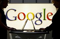Insignia de Google frente a dos personas que utilizan ordenadores