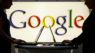 Insignia de Google frente a dos personas que utilizan ordenadores