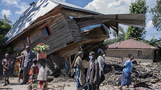 أناس يمشون بالقرب من أحد المنازل المتضررة جراء الفيضانات في نياموكوبي - جمهورية الكونغو الديمقراطية. 2023/05/06