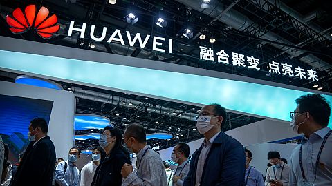 Visitors walk past a booth for Chinese technology firm Huawei at the PT Expo in Beijing, 2021