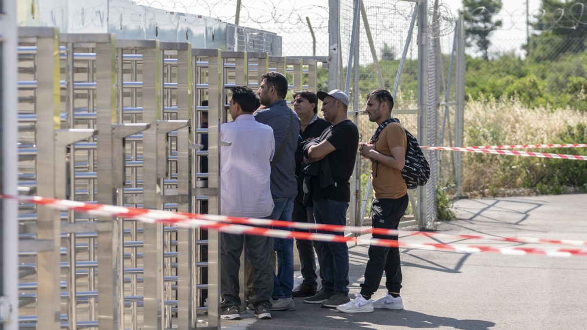 A group of men wait at the turnstiles and speak with survivors, mostly from Pakistan, of a deadly migrant boat sinking at a migrant camp in Malakasa north of Athens, on Monday