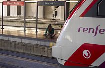 Una joven espera sentada en un andén junto a un tren de Renfe, Atocha, Madrid