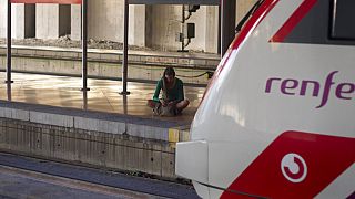 Una joven espera sentada en un andén junto a un tren de Renfe, Atocha, Madrid