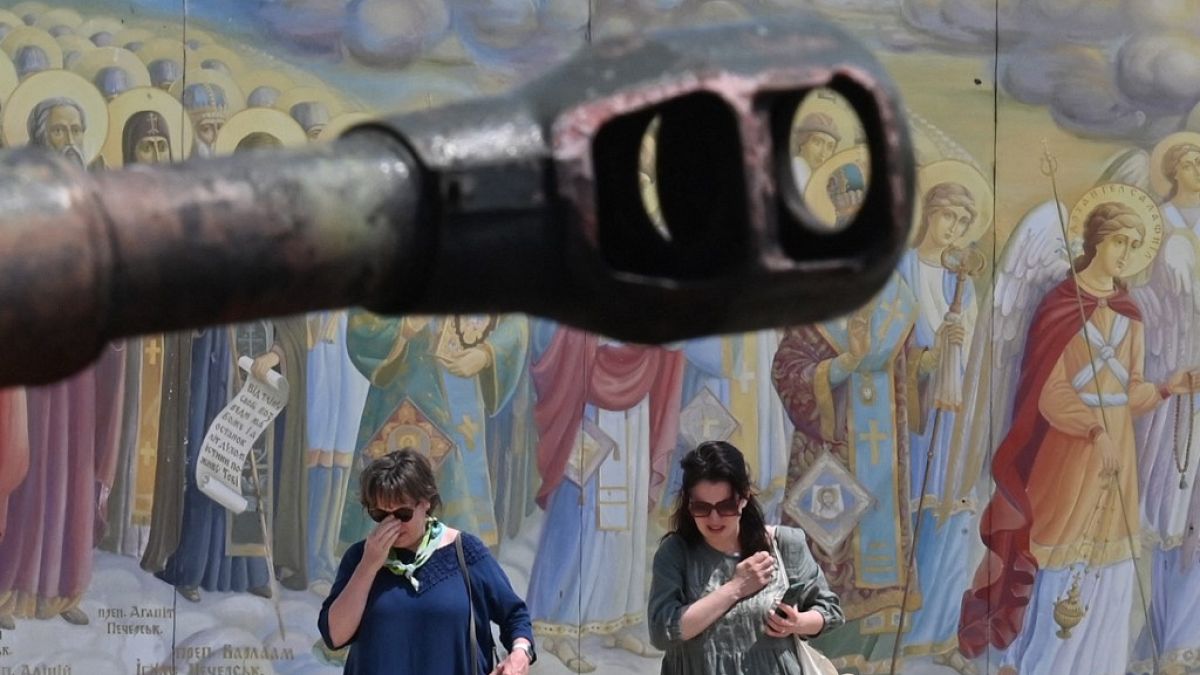 Women cross themselves as they walk by Mykhaylo Golden Domed cathedral frescoes and new exhibits of open air exhibition of destroyed Russian armoured vehicles in Kyiv in June.
