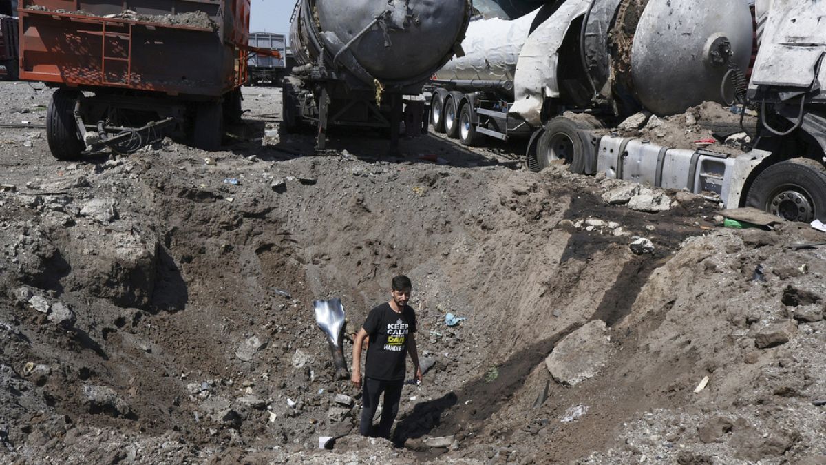 Homem dentro de uma cratera junto a camiões destruídos, após bombardeamento russo em Rozumivka, perto de Zaporíjia, Ucrânia