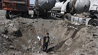 Homem dentro de uma cratera junto a camiões destruídos, após bombardeamento russo em Rozumivka, perto de Zaporíjia, Ucrânia
