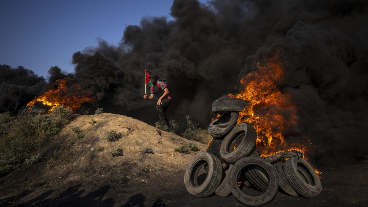 Palestinians burn tires and wave the national flag during a protest against an Israeli military raid in the West Bank city of Jenin, along the border fence with Israell.