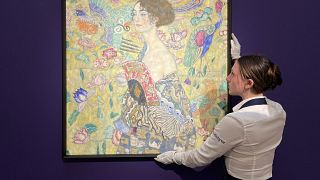 An employee poses with an artwork entitled 'Dame mit Facher (Lady with a Fan)' by Austrian artist Gustav Klimt, at Sotheby's auction house in central London.