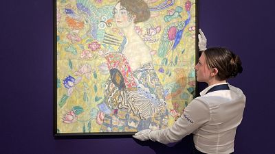 An employee poses with an artwork entitled 'Dame mit Facher (Lady with a Fan)' by Austrian artist Gustav Klimt, at Sotheby's auction house in central London.